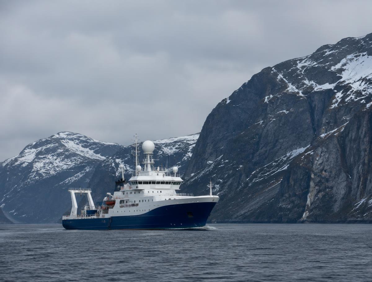 Civilian research vessel with radar domes sailing along a snow-covered Norwegian fjord